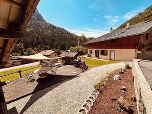 A wooden deck with outdoor furniture, a gravel path, and a view of a mountain and forest. - Semi-detached mountain chalet with fireplace (Bellevaux)