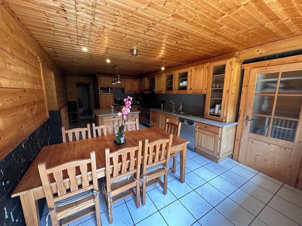 Ein Holzinterieur mit einem Esstisch und Stühlen, einer Küchenzeile mit Schränken und einem Fenster sowie einem gefliesten Boden.
