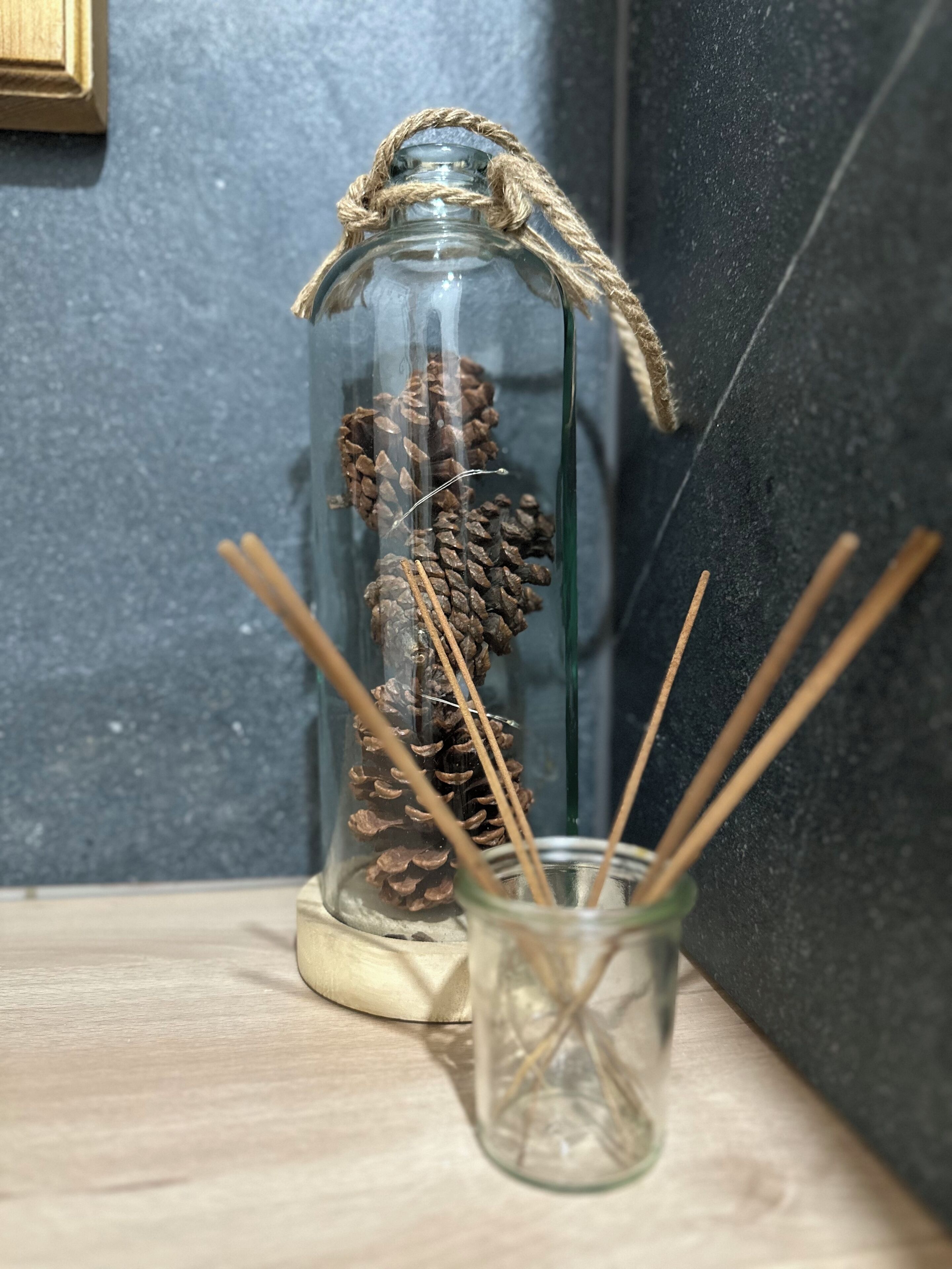 A glass jar with pine cones and reed sticks on a wooden shelf.