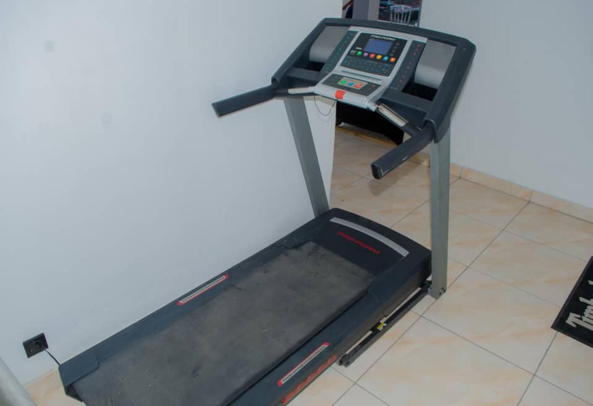 A treadmill in a room with tiled flooring and a white wall.