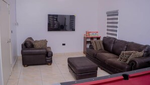 A living room with two brown leather sofas, a coffee table, a television mounted on the wall, and a Monopoly board game on a shelf. - Bamgbose Apartments in Surulere, Lagos Nigeria (Lagos)