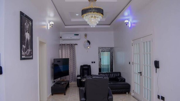 A living room with a black leather sofa, a black armchair, a flat-screen TV, a ceiling fan, and a chandelier. - Bamgbose Apartments in Surulere, Lagos Nigeria (Lagos)