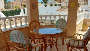 A covered outdoor seating area with wicker chairs and a table, overlooking a residential neighborhood. - Costa Blanca Luxury villa with private pool on exclusive development (San Miguel de Salinas)