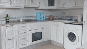 A compact kitchen with white cabinetry, a built-in oven, a washing machine, and a countertop with a coffee maker and a bottle. - Costa Blanca Luxury villa with private pool on exclusive development (San Miguel de Salinas)