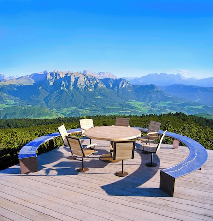A wooden deck with a round table and chairs, overlooking a mountainous landscape.
