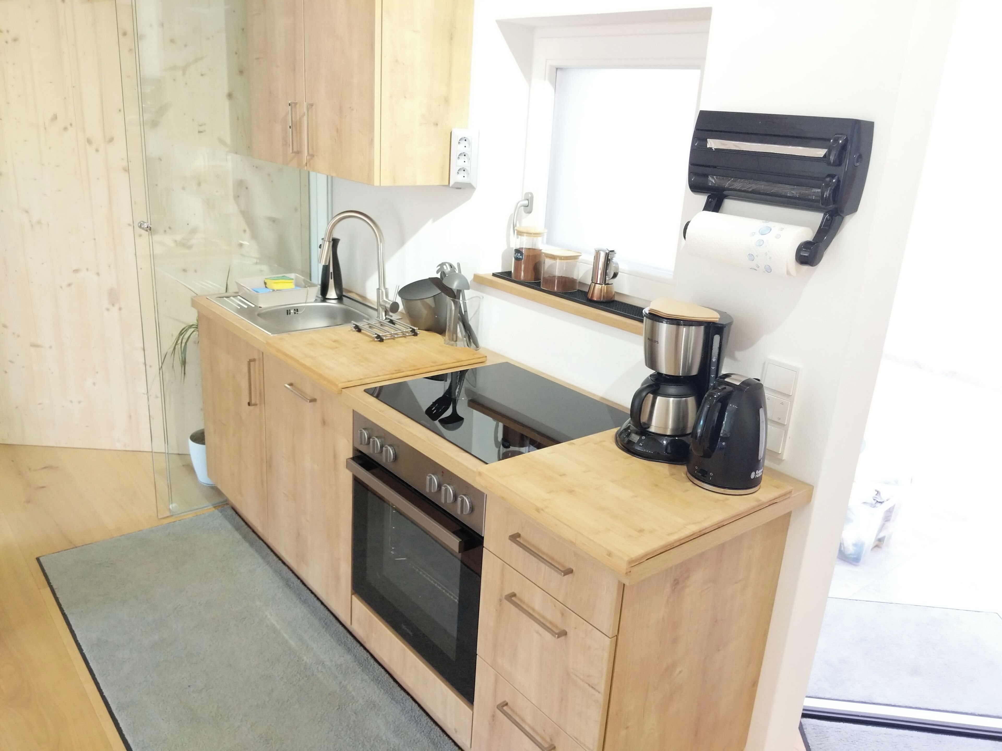 A compact kitchen with wooden cabinets, a built-in oven, a coffee maker, and a sink.