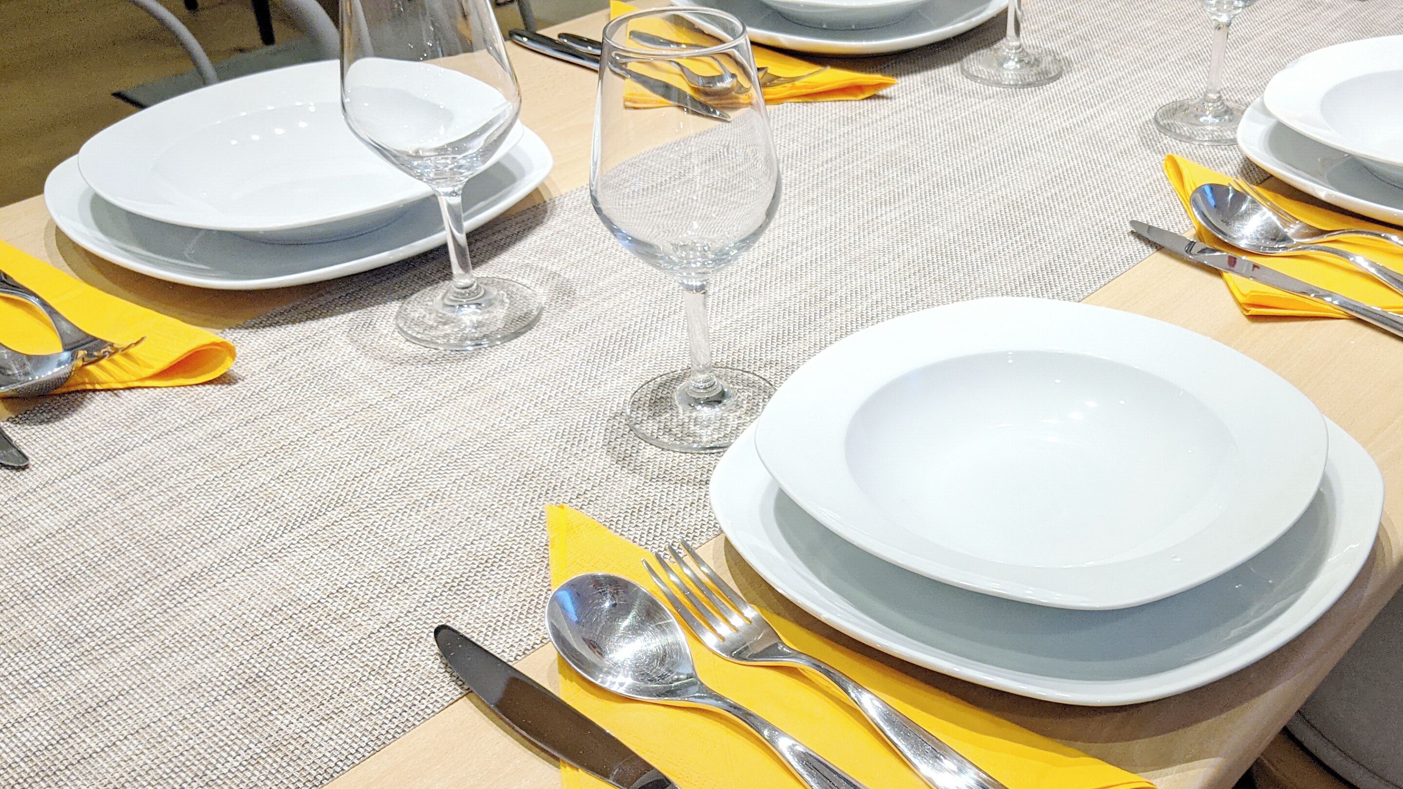 Une table dressée avec des assiettes, des couverts et des verres à vin, ce qui indique une mise en place pour un repas formel.