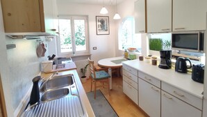 A modern kitchen with a sink, stove, and microwave. There is a dining table with chairs and a window with a view of trees. - Vidora Apartments - Dolomites relaxing Skyline Retreat (Ritten)