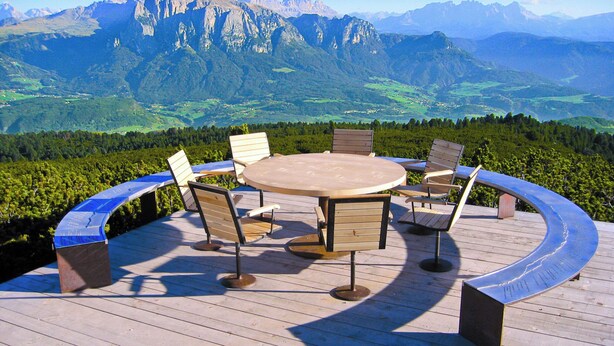 Una terraza de madera con una mesa redonda y sillas, con vista a un paisaje montañoso.