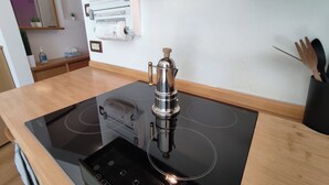 Una cocina con una placa de inducción negra, una cafetera de acero inoxidable y un horno empotrado.