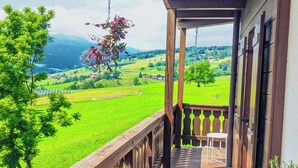 A balcony with a wooden railing, a white chair, and a hanging plant.