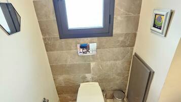 A bathroom with a toilet, a shower, a sink, a window, and a towel rack.
