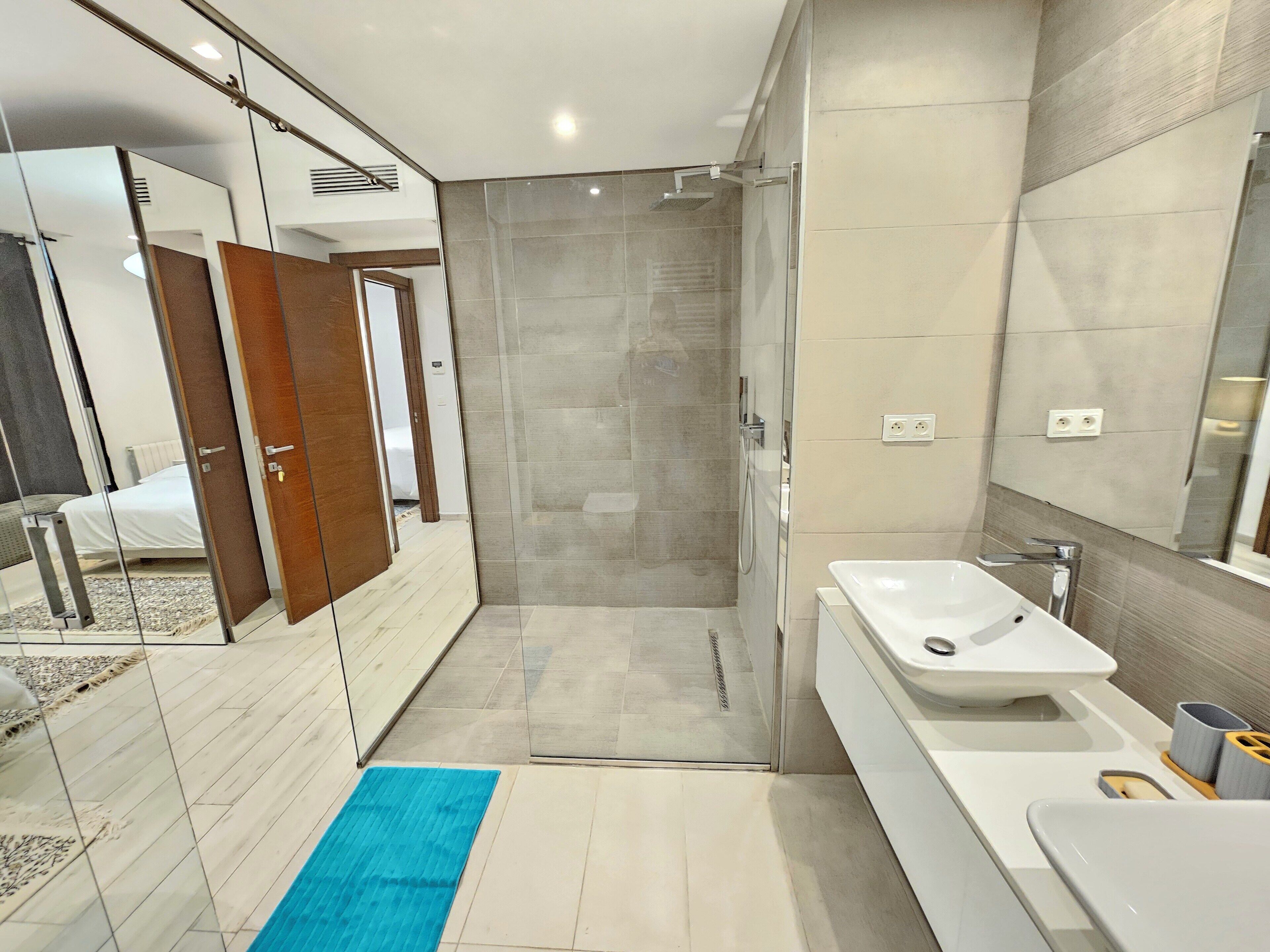 Un baño moderno con ducha de vidrio, lavamanos blanco y un espejo grande.