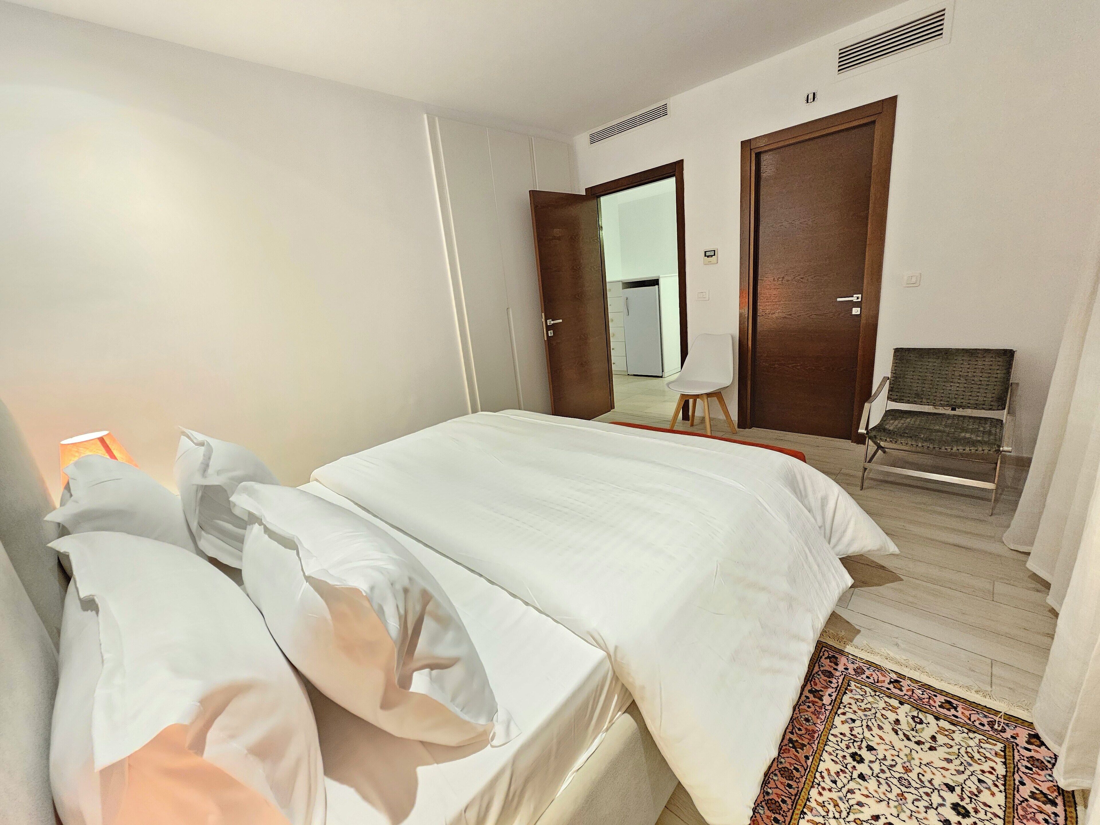 Quarto de hotel com uma cama, uma cadeira, um abajur e uma porta para um banheiro.