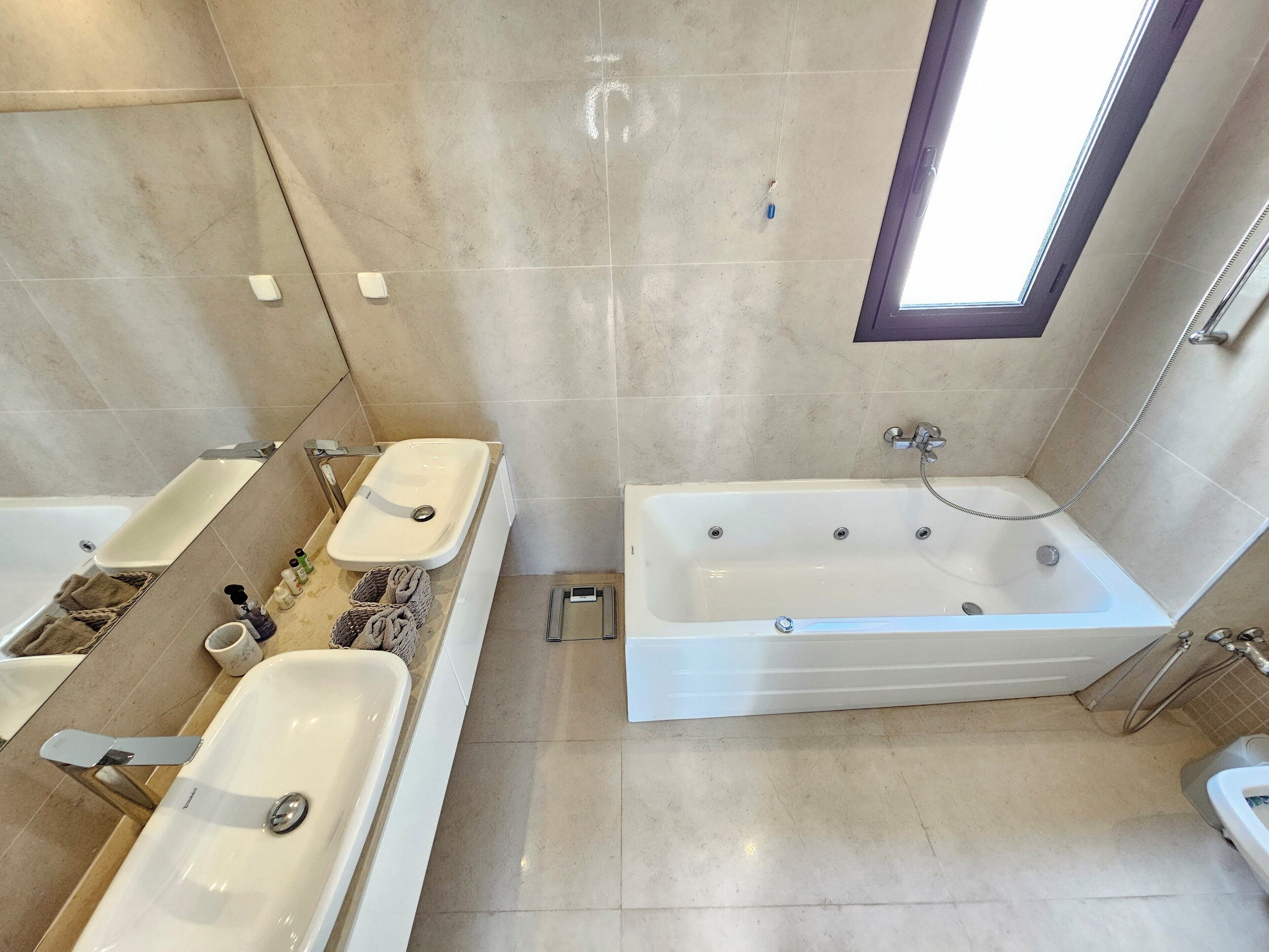 A modern bathroom with a bathtub, two sinks, and a window.