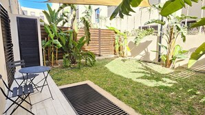 Een patio met een tafel en stoelen, een betonnen vloer, een gazon en een groot zonnescherm.