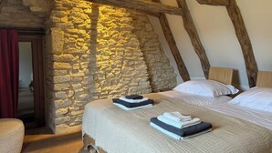 A bedroom with a stone wall, wooden beams, a bed with white linens, and a red curtain.