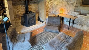 A rustic stone fireplace with a wood-burning stove, a small table, and two cushioned chairs in a cozy room.