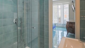 Un baño moderno con ducha de vidrio, lavamanos y vistas al balcón exterior.