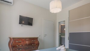 Un dormitorio con una cama, un aparador de madera, un televisor y un baño a la vista a través de una puerta abierta.