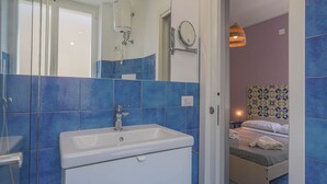 Un baño con lavamanos blanco, azulejos azules, ducha y espejo.