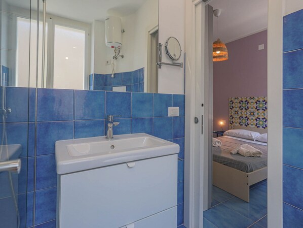 Un baño con lavamanos blanco, azulejos azules, ducha y espejo.