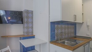 Una cocina compacta con televisor integrado, un pequeño comedor y un lavamanos.