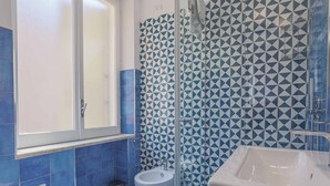 Un baño con azulejos azules, un lavamanos blanco y una cabina de ducha de cristal.