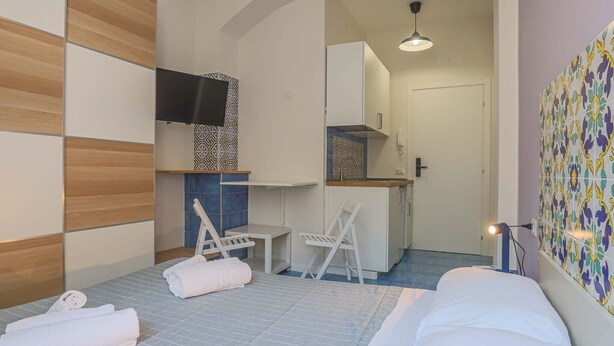 Habitación de hotel con cama, escritorio, silla, televisión y zona de cocina.