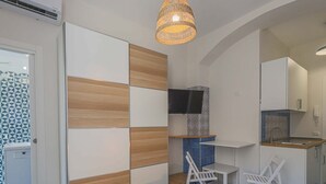 Habitación de hotel con cama, televisor montado en la pared, una pequeña cocina y un rincón de estar con sillas.