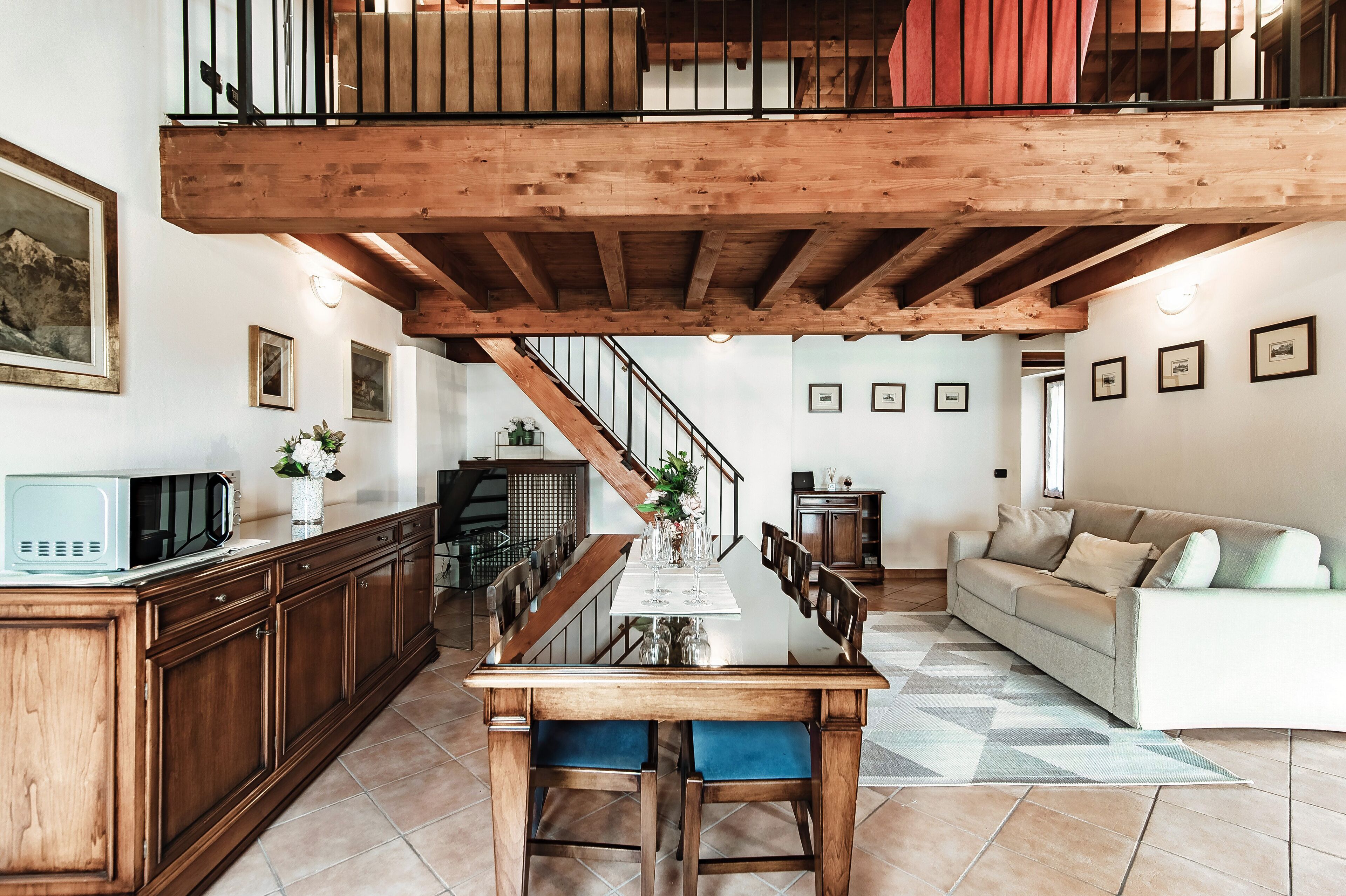 A spacious living area with a wooden dining table, a sofa, and a staircase leading to an upper level.