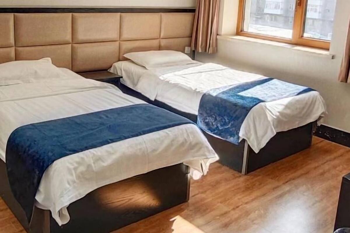 A hotel room with two beds, a window with curtains, and a wooden floor.