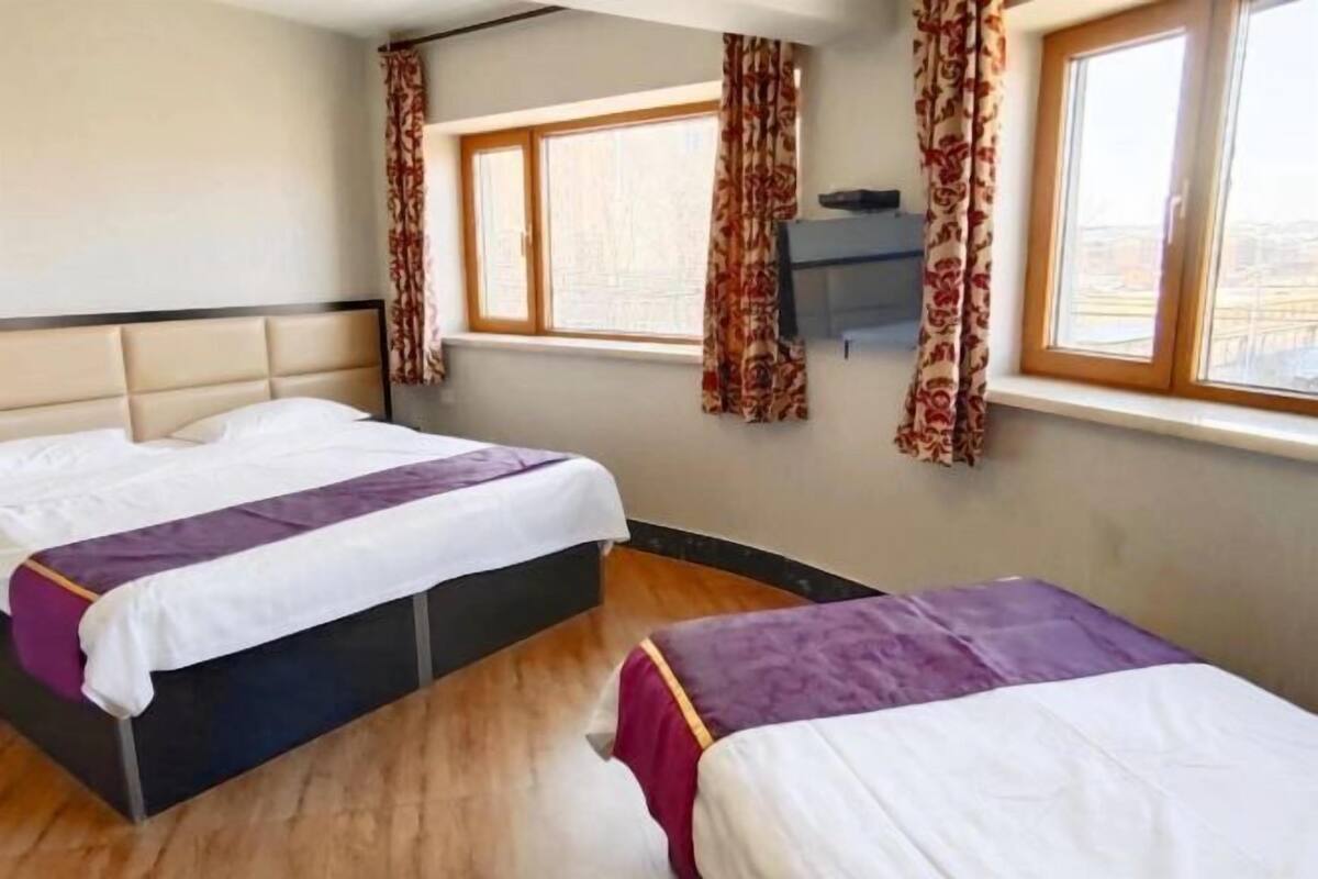 A room with two beds, a window with curtains, and a wooden floor.