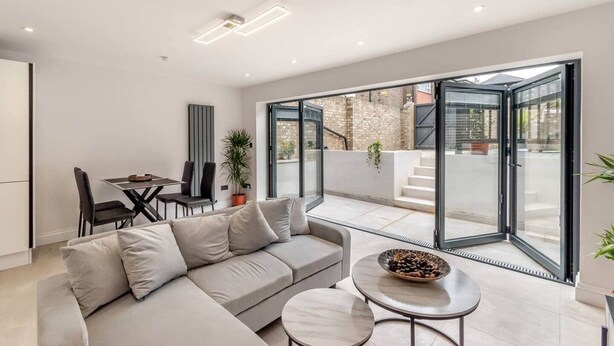 Un soggiorno moderno con divano, tavolo da pranzo e sedie, un balcone con vista sulla città e un'ampia porta scorrevole in vetro.