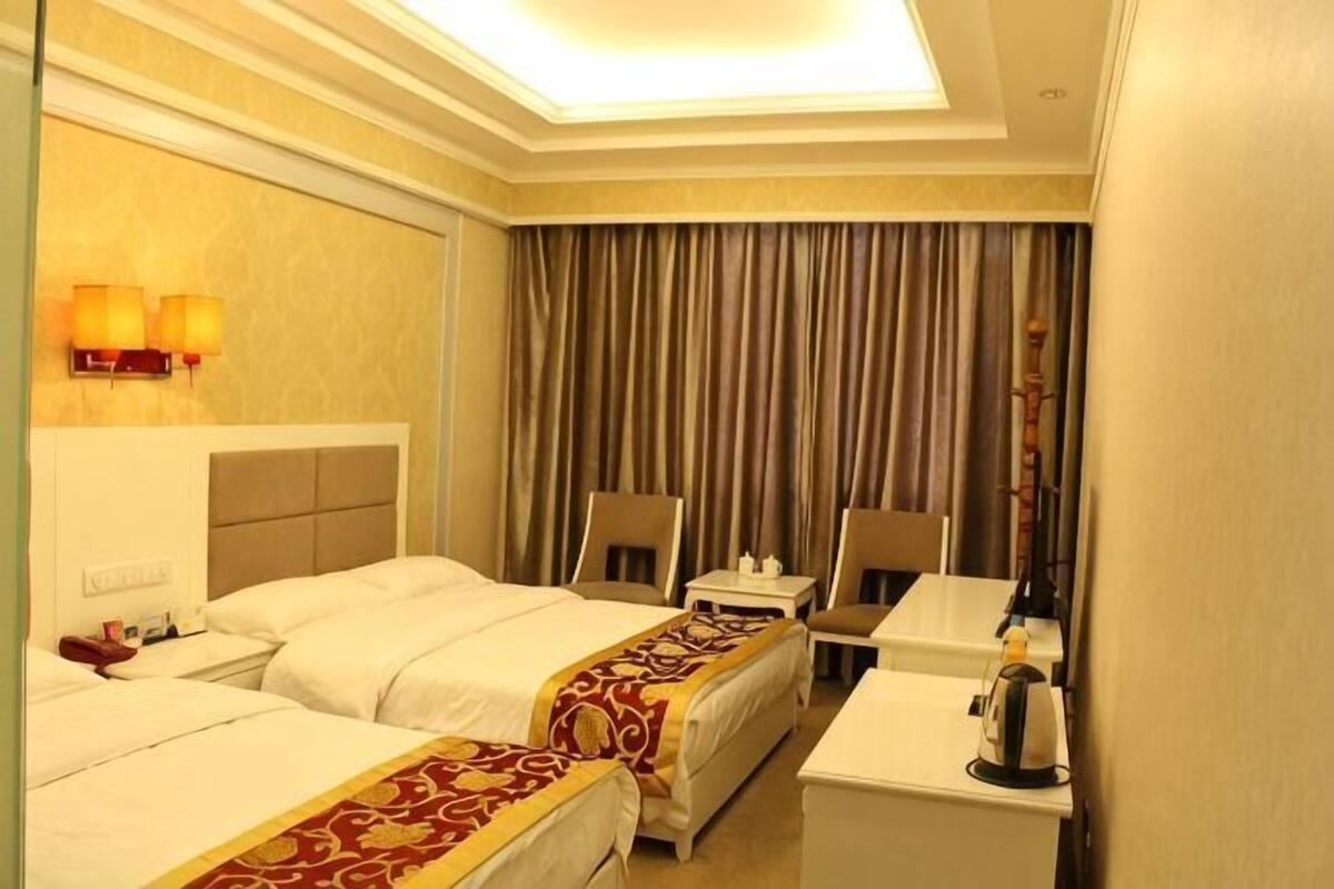 Een hotelkamer met twee bedden, een bureau, een stoel, een lamp en een raam met gordijnen.