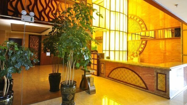 Um lobby com balcão de recepção, plantas em vasos e uma escada com corrimão de madeira.