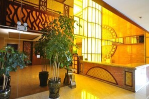 Un vestíbulo con mostrador de recepción, plantas en macetas y una escalera con barandilla de madera.