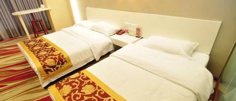 A hotel room with two beds, a red carpet, a white headboard, and a small table with a lamp.