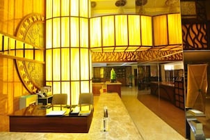 A hotel lobby with a reception desk, chairs, and a large decorative wall.