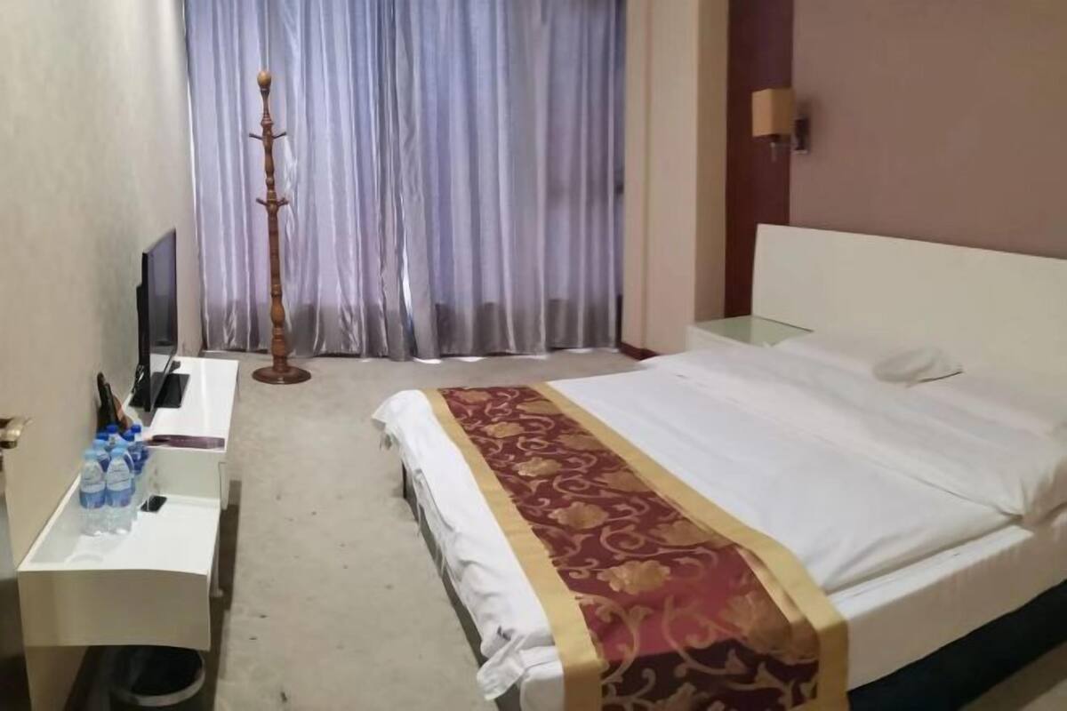 Een hotelkamer met een bed, een bureau met een computer en waterflesjes, een lamp en een gordijn.