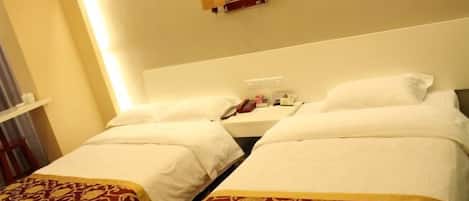 A hotel room with two beds, each with a white bedspread and a red and gold decorative pillow. There is a nightstand with a lamp and a phone.