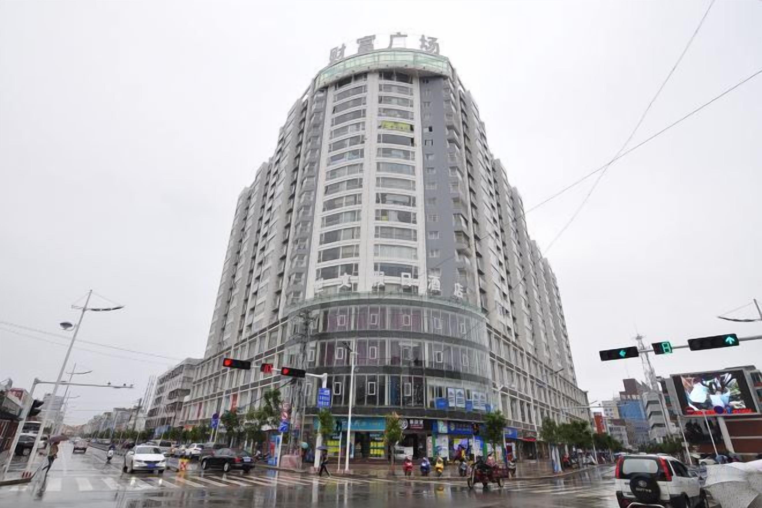 Un edificio de varios pisos con fachada curva, situado en una concurrida intersección con semáforos y señales de tráfico.