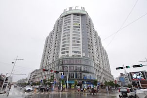 Un edificio de varios pisos con fachada curva, situado en una concurrida intersección con semáforos y señales de tráfico.