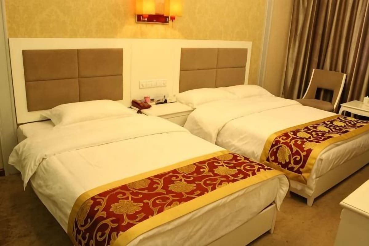 Habitación de hotel con dos camas, una mesita de noche, una lámpara y una silla.