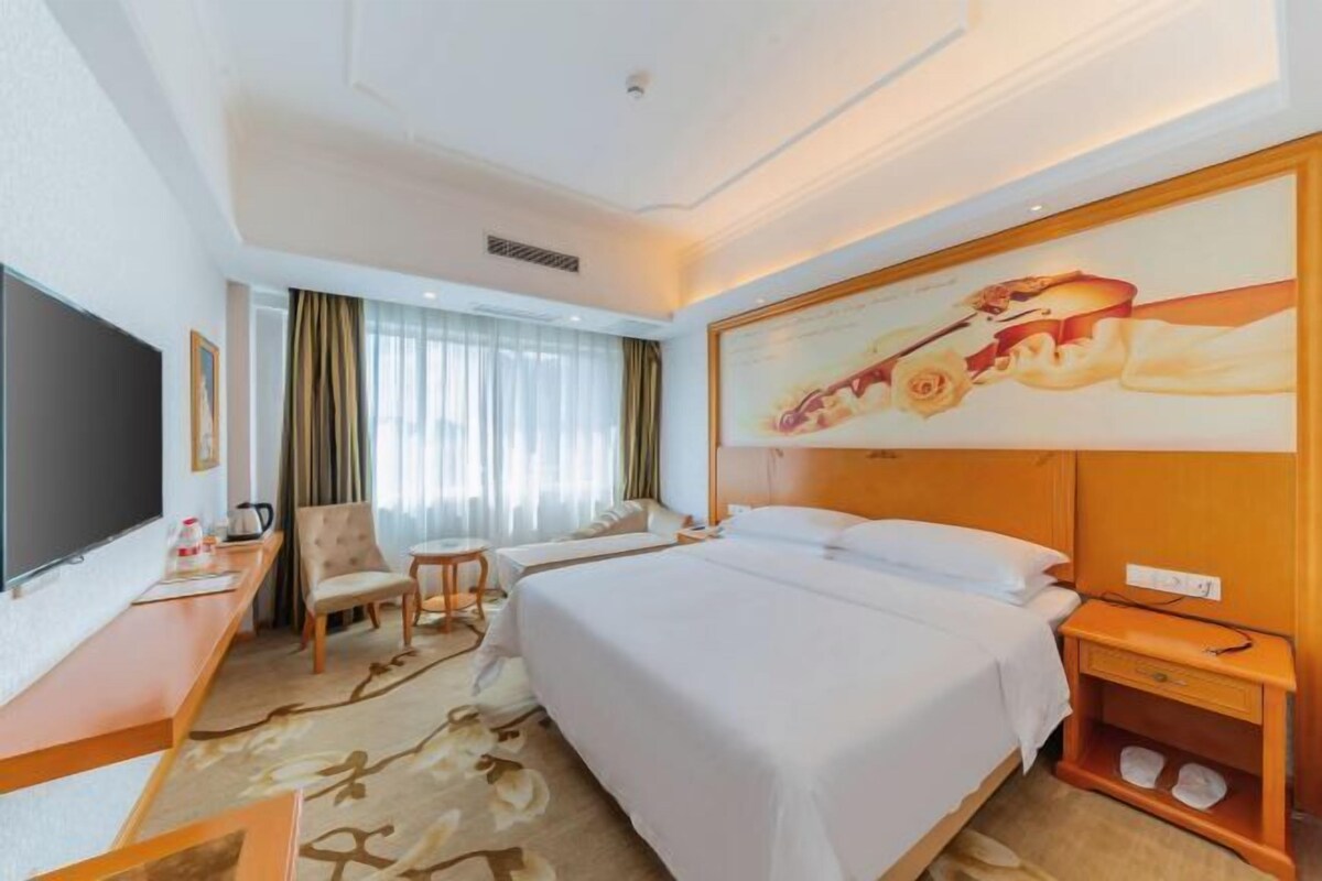 Ein Hotelzimmer mit Bett, Schreibtisch, Stuhl, Fernseher und einem Bild an der Wand.