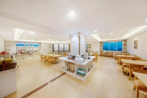 A spacious dining area with multiple tables and chairs, a central serving station, and large windows providing natural light.