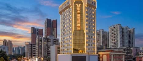 Un hotel de varios pisos con un letrero vertical llamativo, rodeado de otros edificios altos.