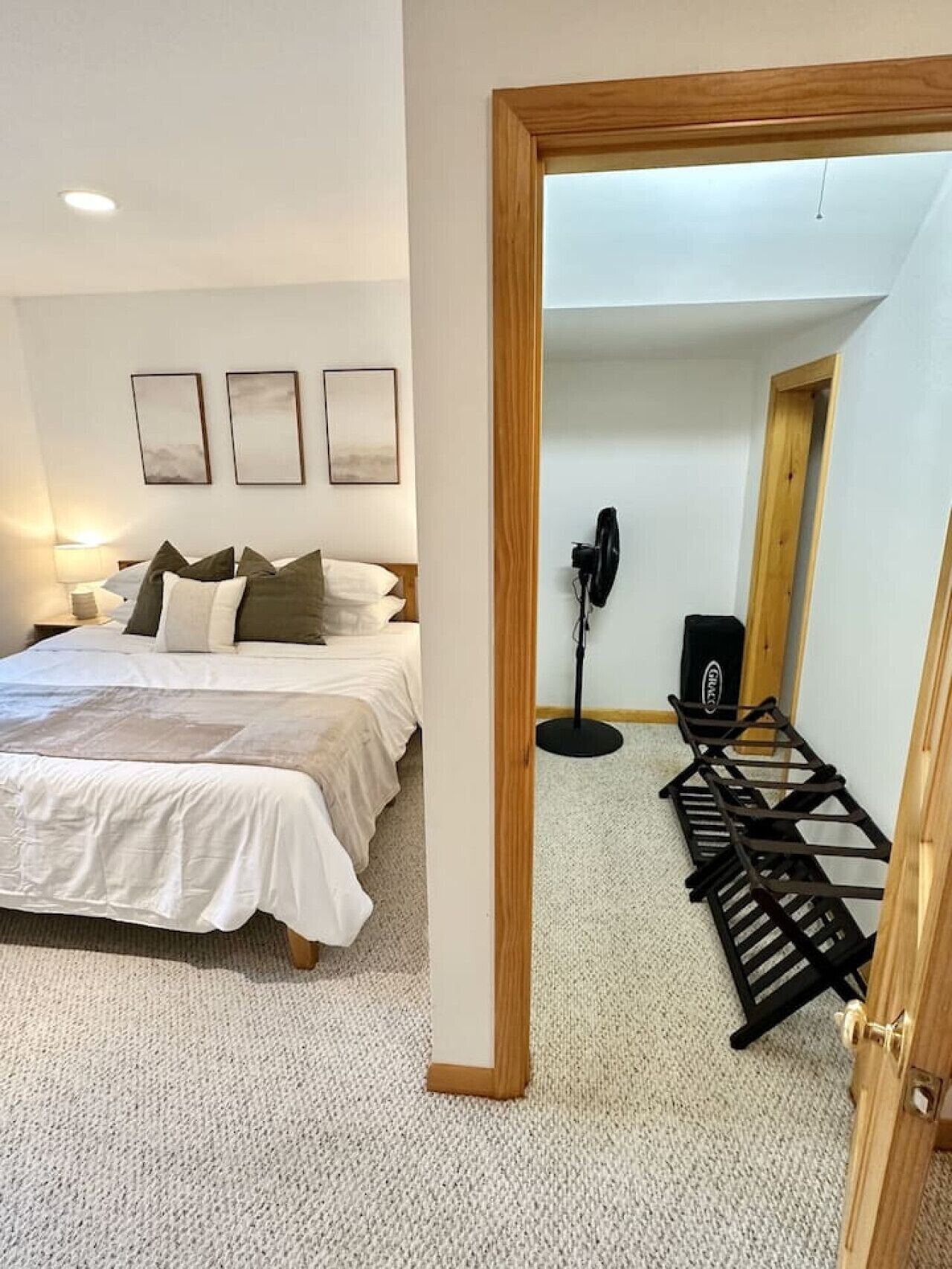 A bedroom with a bed, bedside lamps, a standing fan, and a wooden door.
