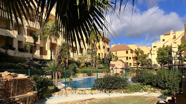 Ein Poolbereich eines Resorts, mit klarem Pool, umgeben von Palmen und einem Zaun.