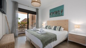 Ein modernes Hotelzimmer mit einem großen Bett, einem Holz-Kopfteil, einer grünen Tagesdecke, einem Korbstuhl, einem Nachttisch und einem Bild an der Wand.